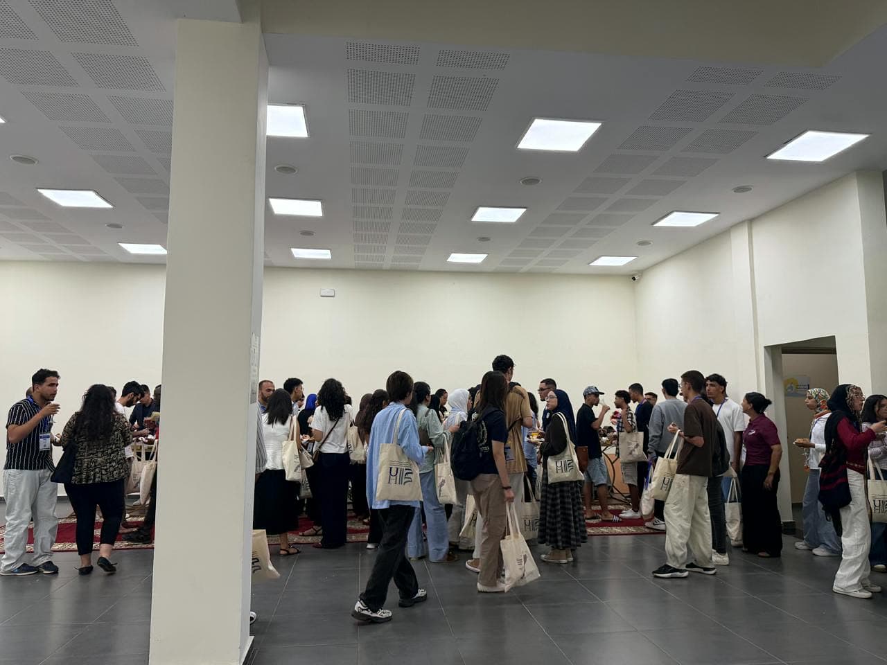 Participants with their welcome tote bags mingling at the evening reception in the ENSEM hall.