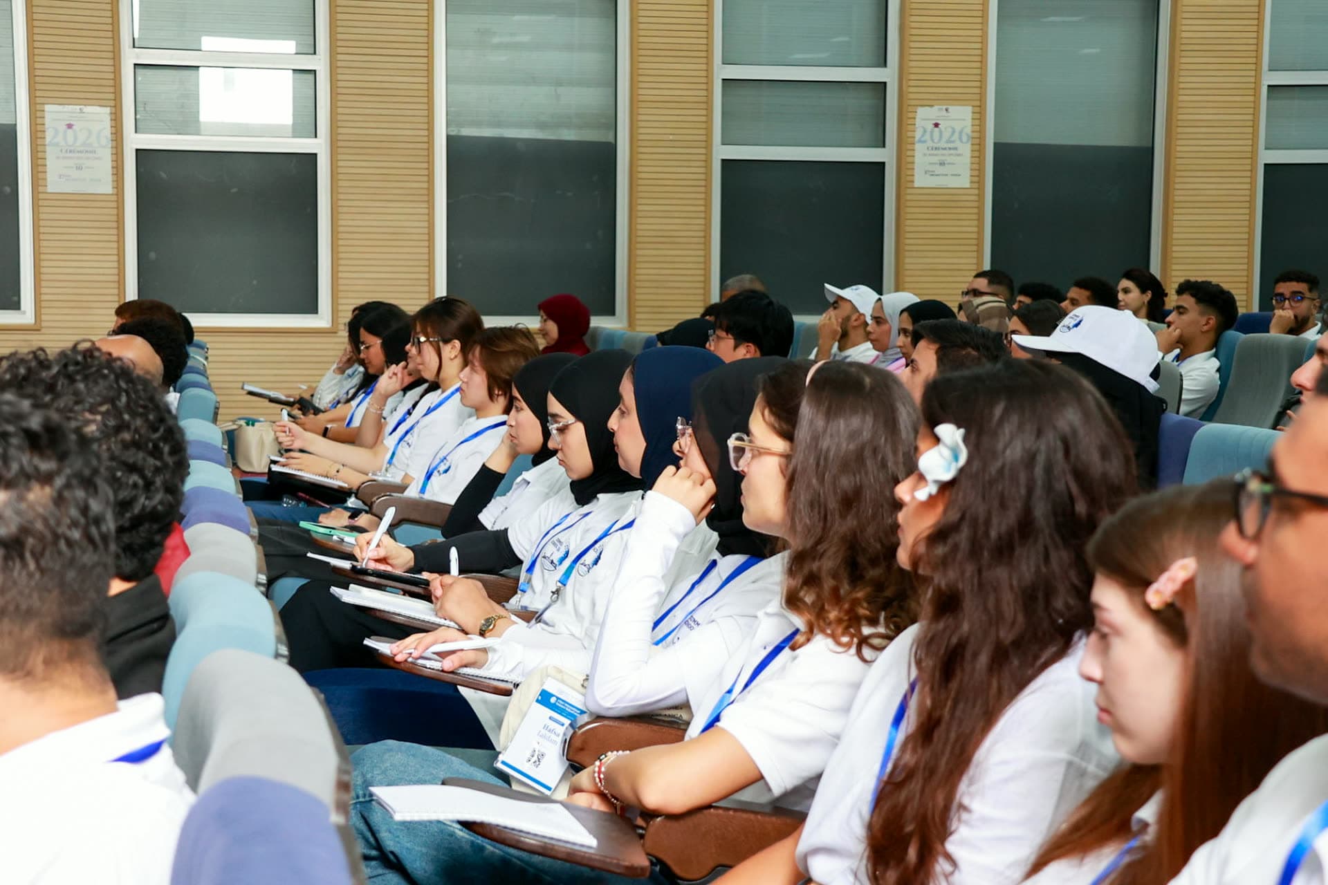 Rows of participants in white cohort polos taking notes during a morning seminar.