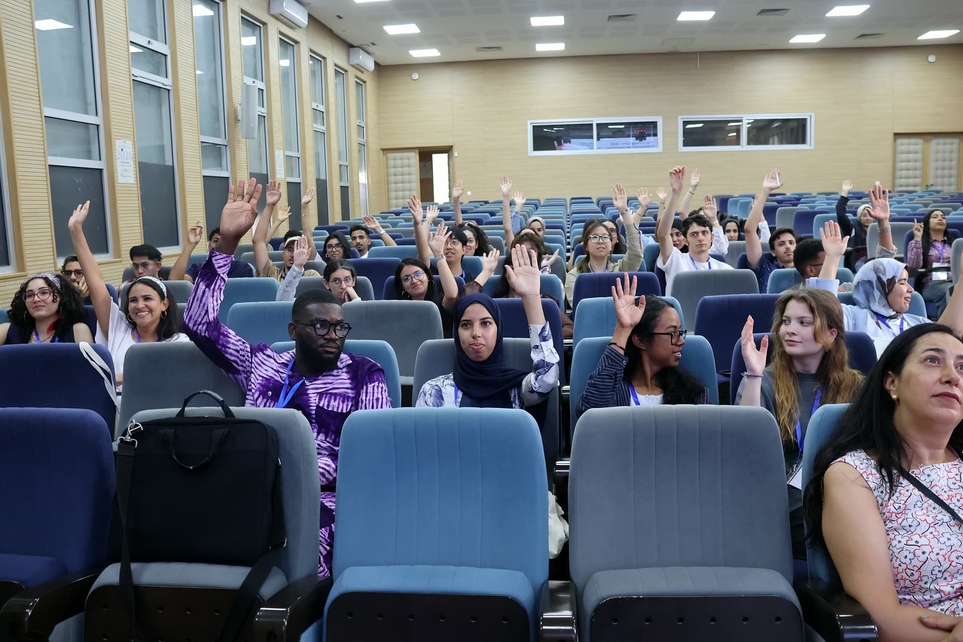 Participants across the auditorium raising their hands during a lecture.