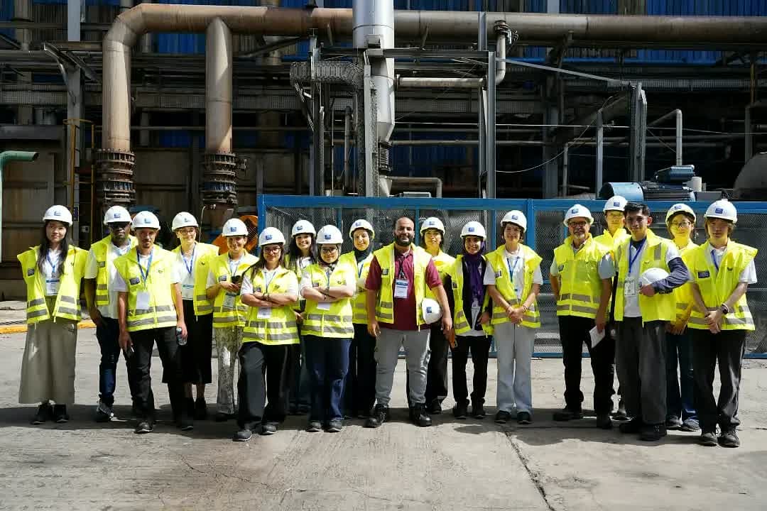 Group photo of the cohort in hard hats and hi-vis vests in front of the Cosumar plant.