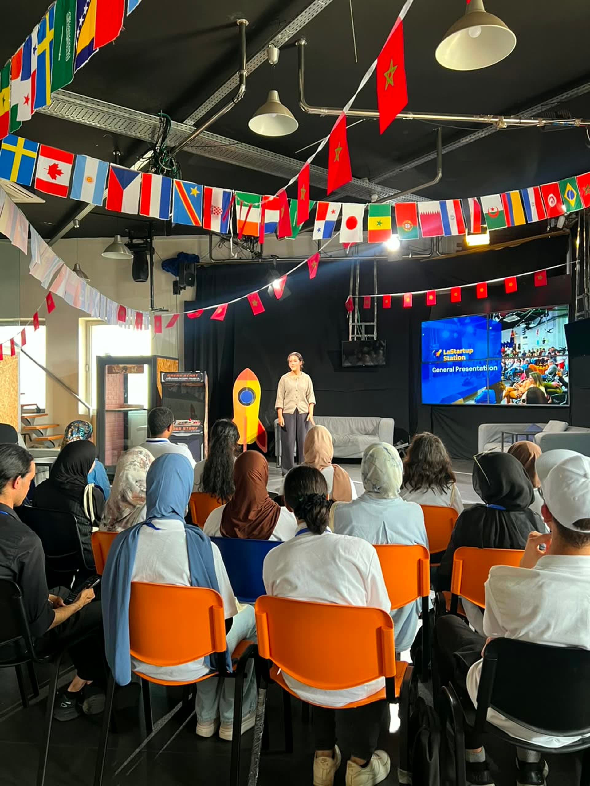 Presentation on the LaStartup Station stage at Technopark Casablanca, country flags hanging overhead.