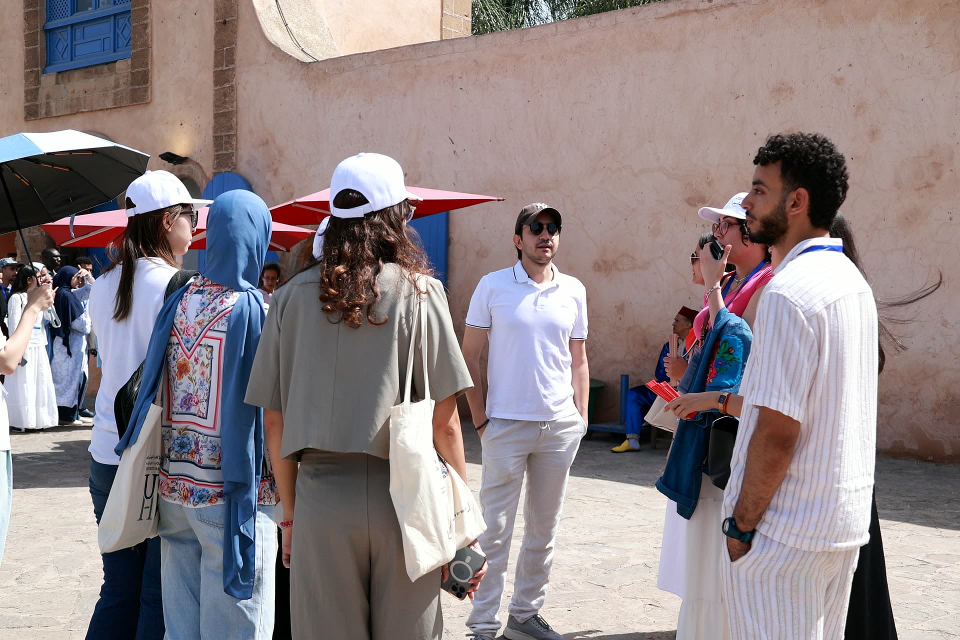 The group gathered with the guide in a medina square, parasols up against the sun.