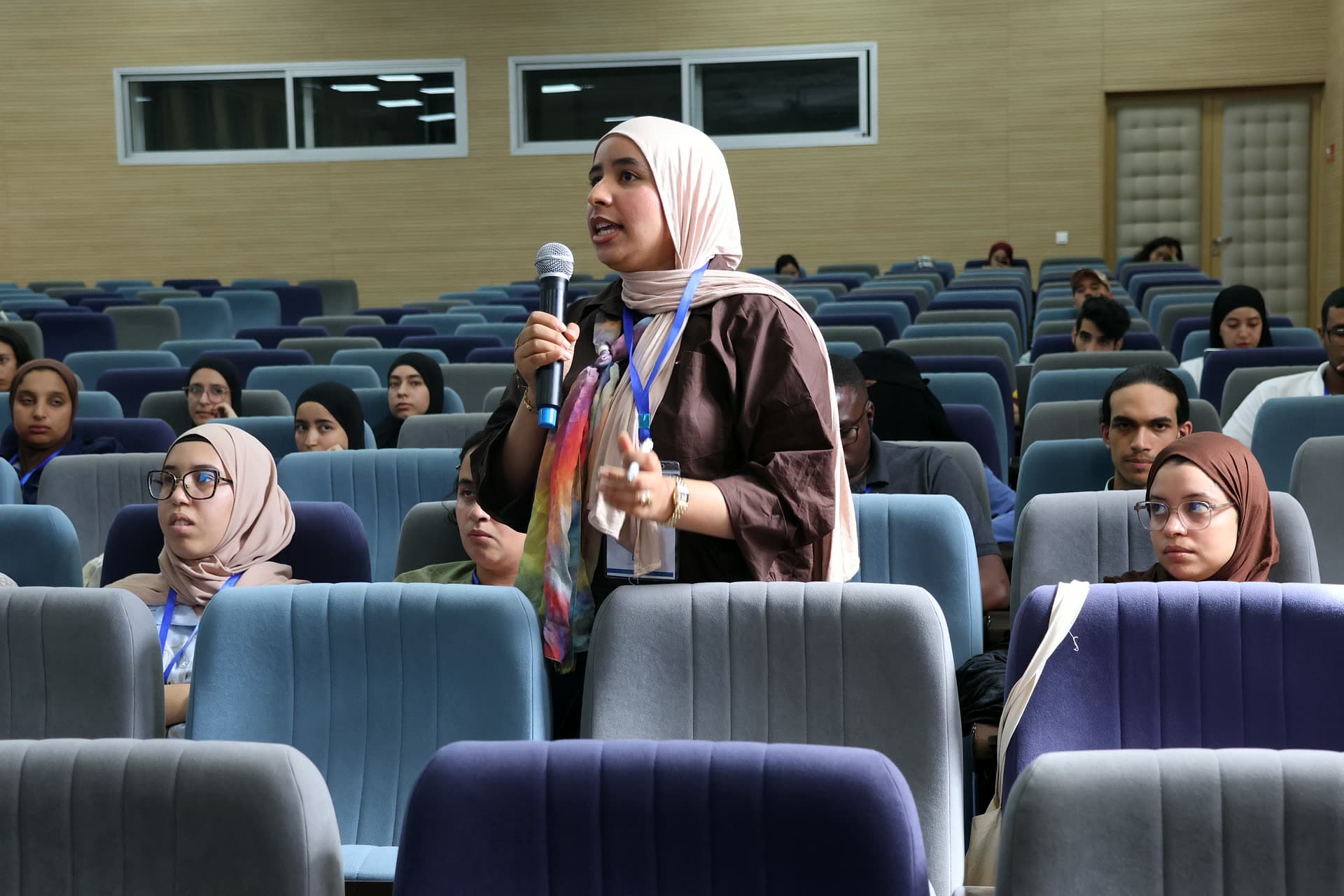 Participant in a colourful scarf standing to ask her question at the microphone.