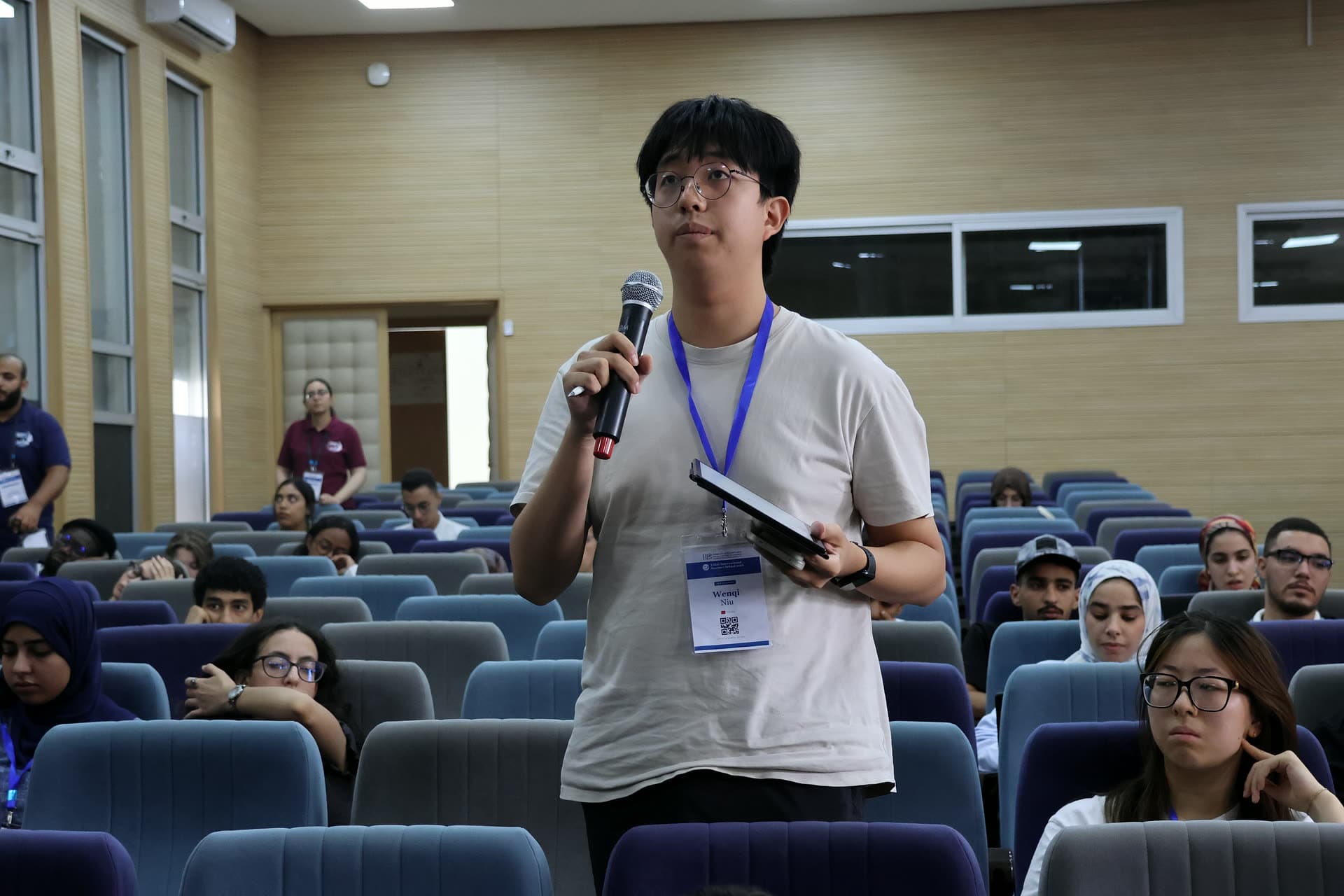 Participant standing with a microphone and notes to ask his question.