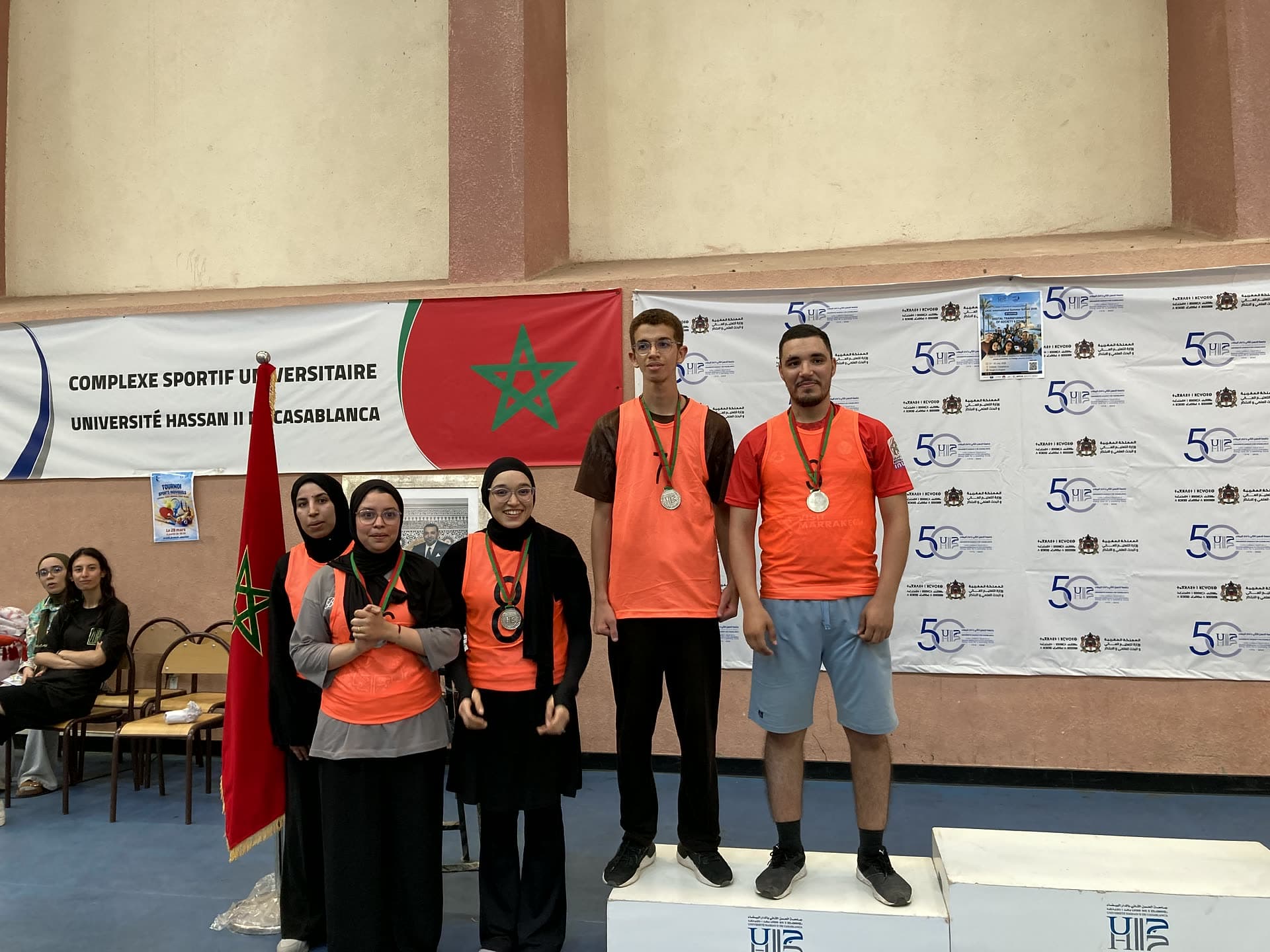 Medalists in orange vests standing on the podium with their medals.