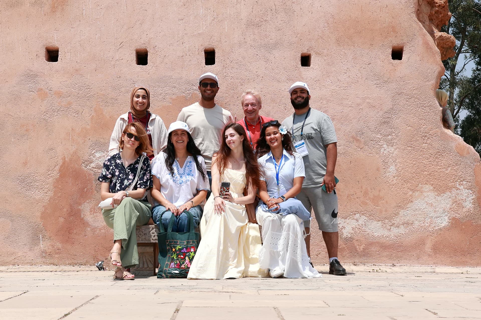 Participants in summer dresses posing at the pink wall of the Kasbah of the Udayas.