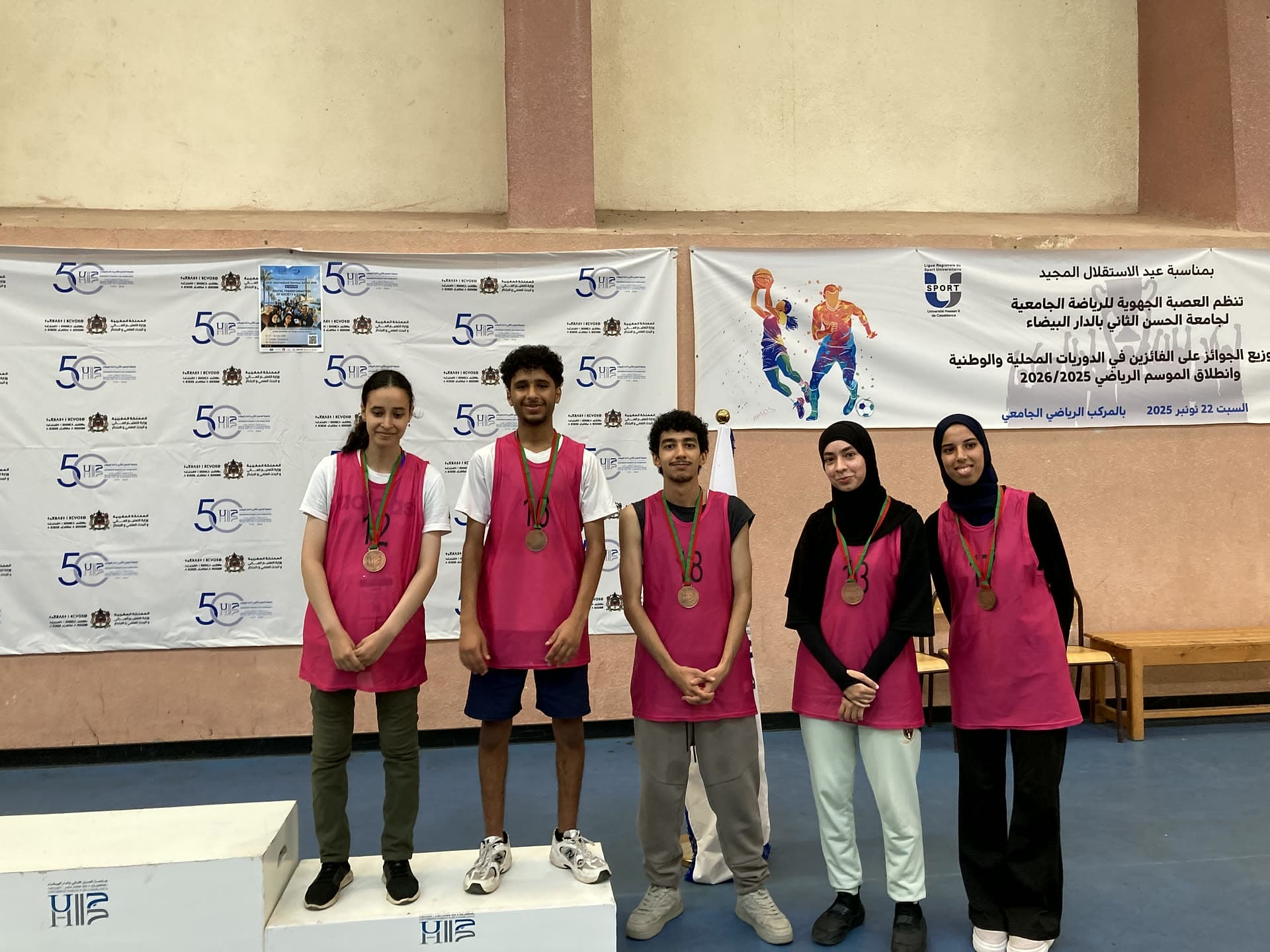 A team in pink vests wearing their medals beside the podium after the sports tournament.
