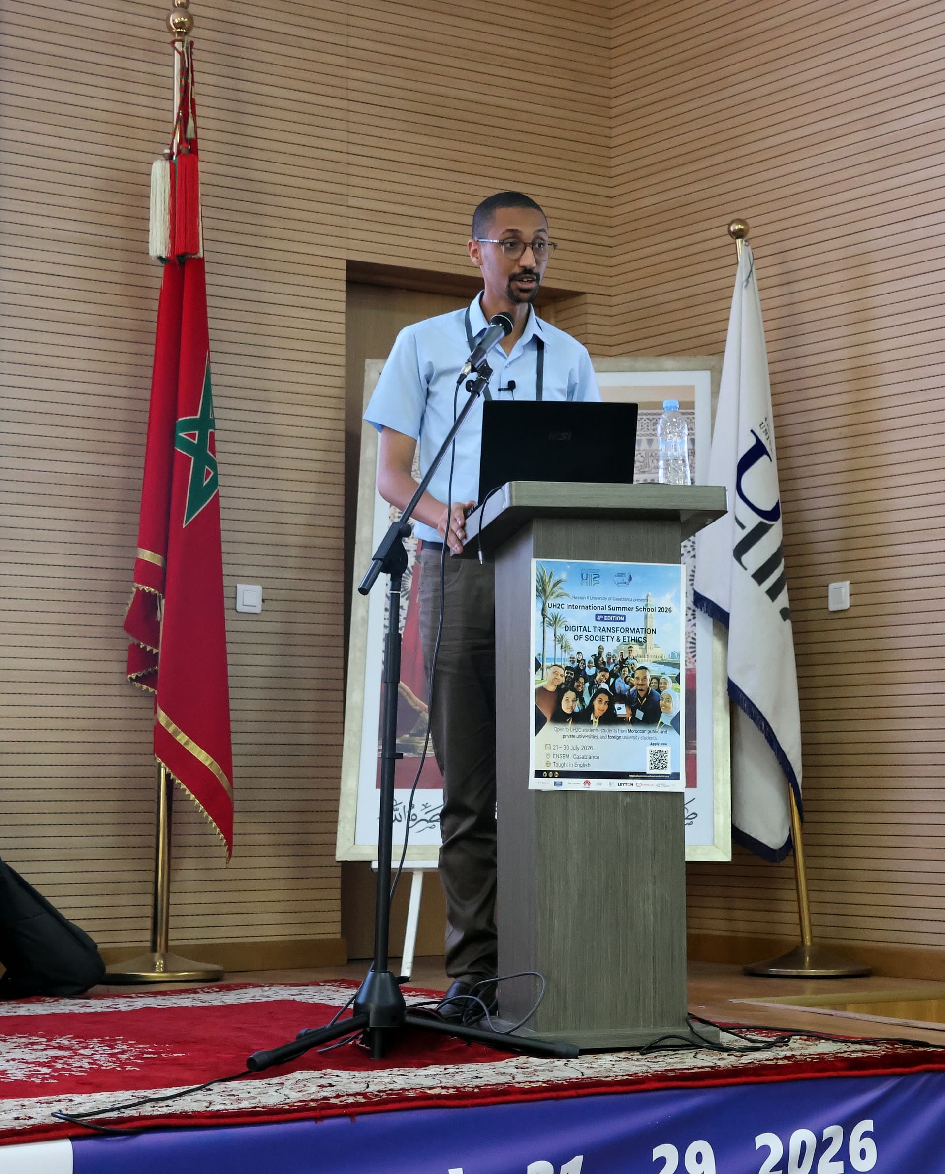 Speaker at the podium beside the Moroccan flag during a morning lecture.