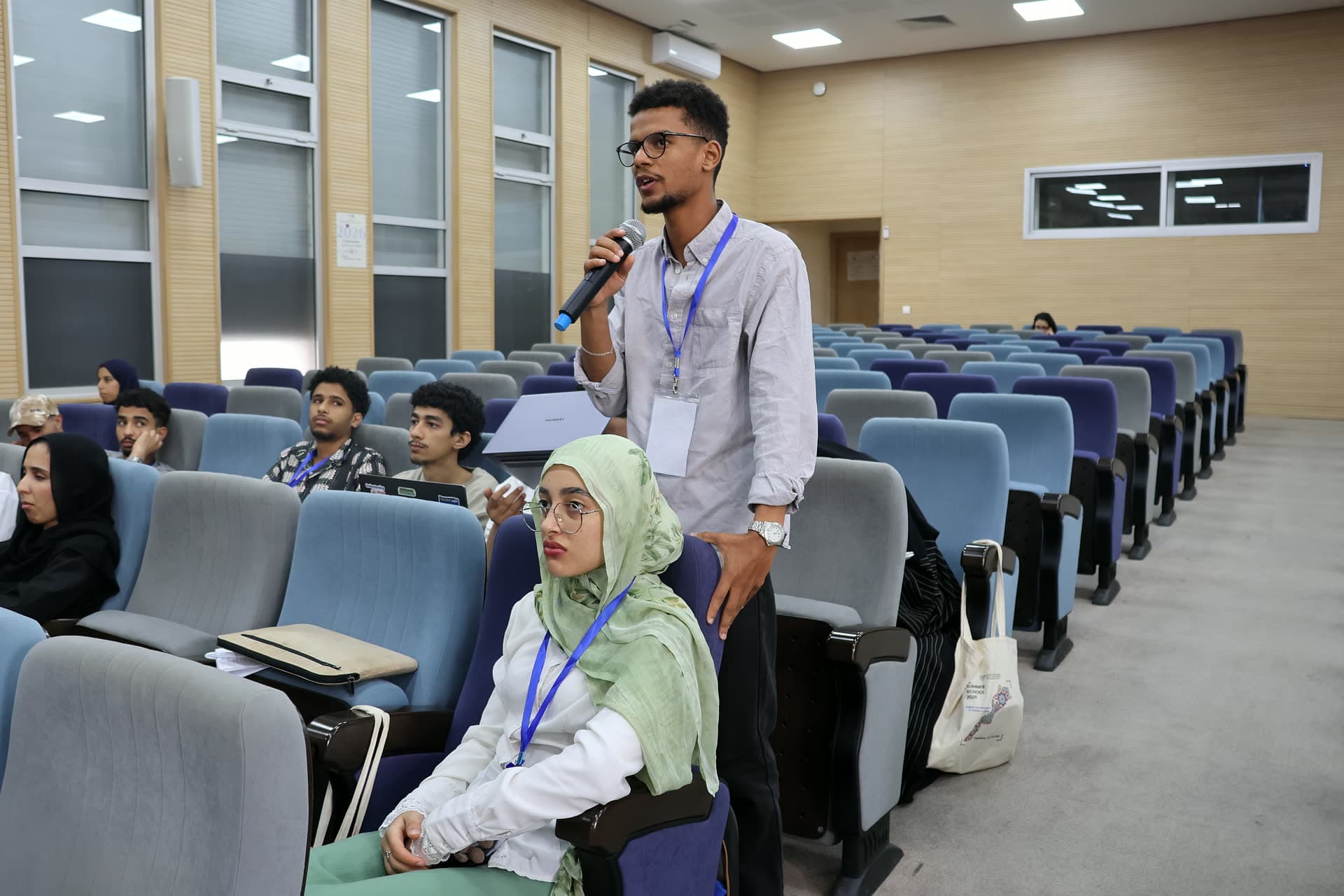A participant standing with the microphone to ask a question, his neighbour listening.