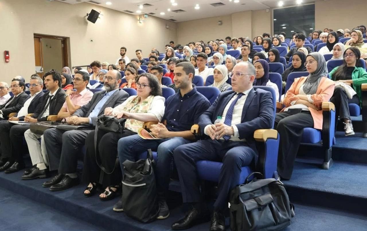 Senior university members in the front row, students filling the auditorium behind.
