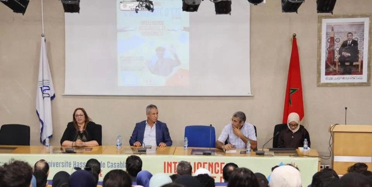 Opening ceremony panel with four facilitators and the Université d'Été poster on the screen.